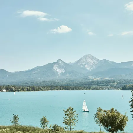 Segelboot auf türkisfarbenem Alpensee vor bewaldeten Bergen